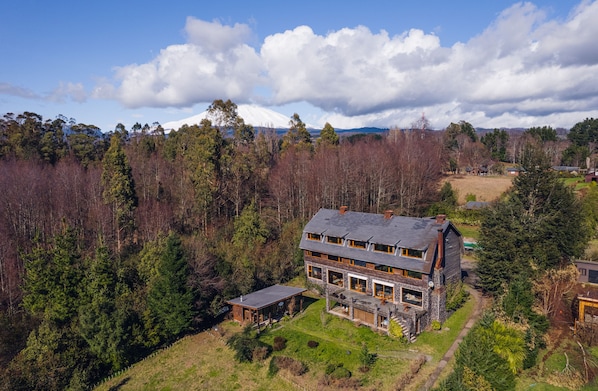 A two-story house with a large front porch, surrounded by a forested area and a mountain in the background. - Hotel CasaEstablo by DOT Boutique (Pucón)