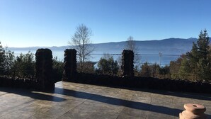 Un camino de piedra que lleva a una terraza con vistas a un cuerpo de agua y montañas a lo lejos.