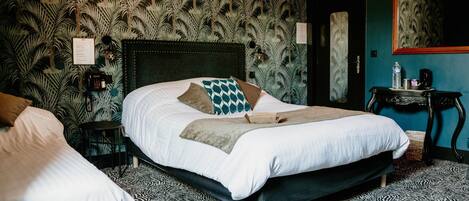 A hotel room with a large bed, a bedside table with a lamp, a telephone, and a wall with a tropical leaf pattern.