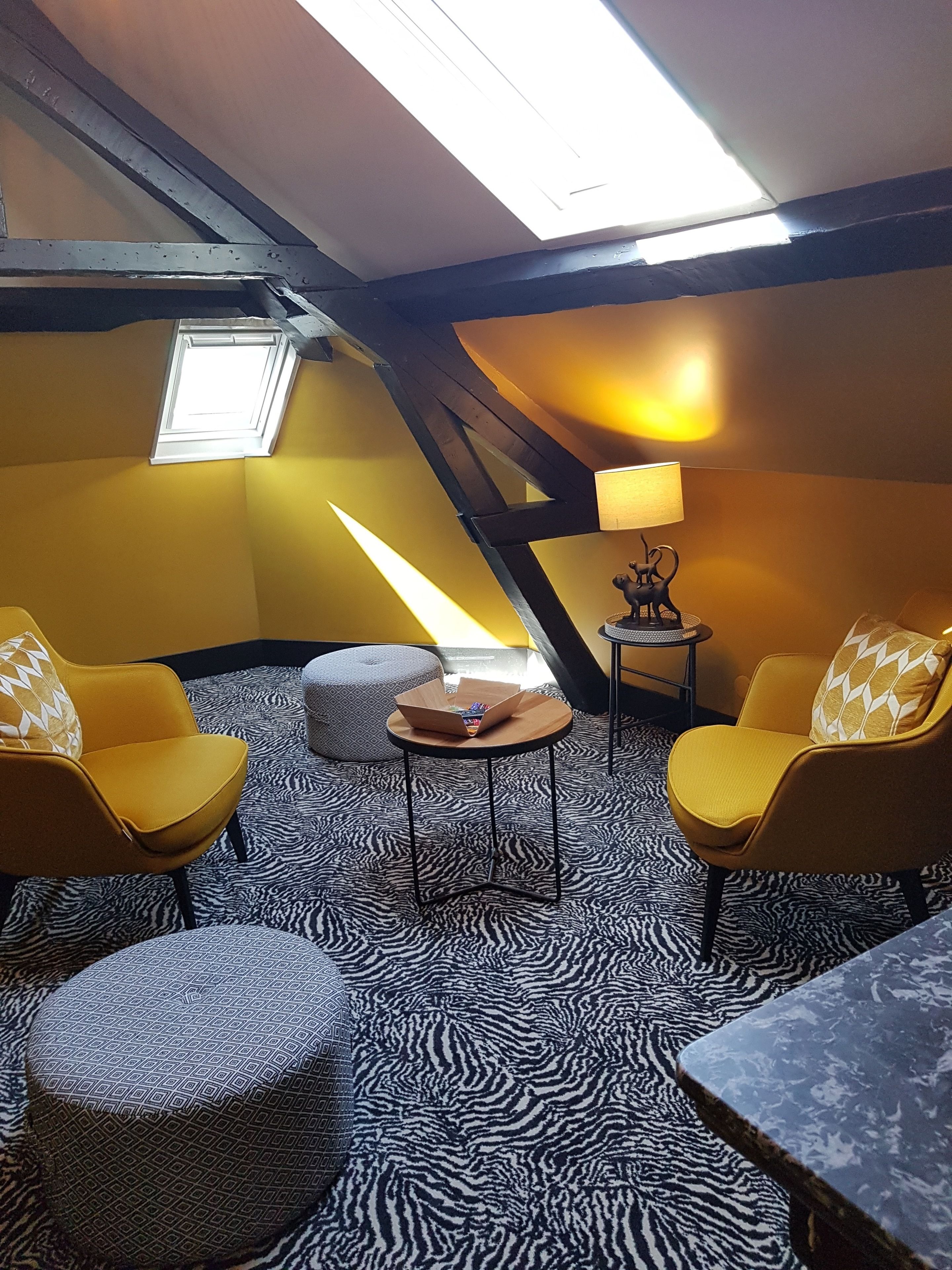 A cozy attic room with yellow walls, a skylight, a zebra-patterned floor, and two yellow armchairs.