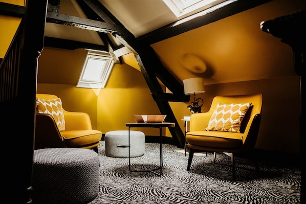 A cozy, yellow-themed room with a sloped ceiling, a small table, two chairs, and a patterned carpet.
