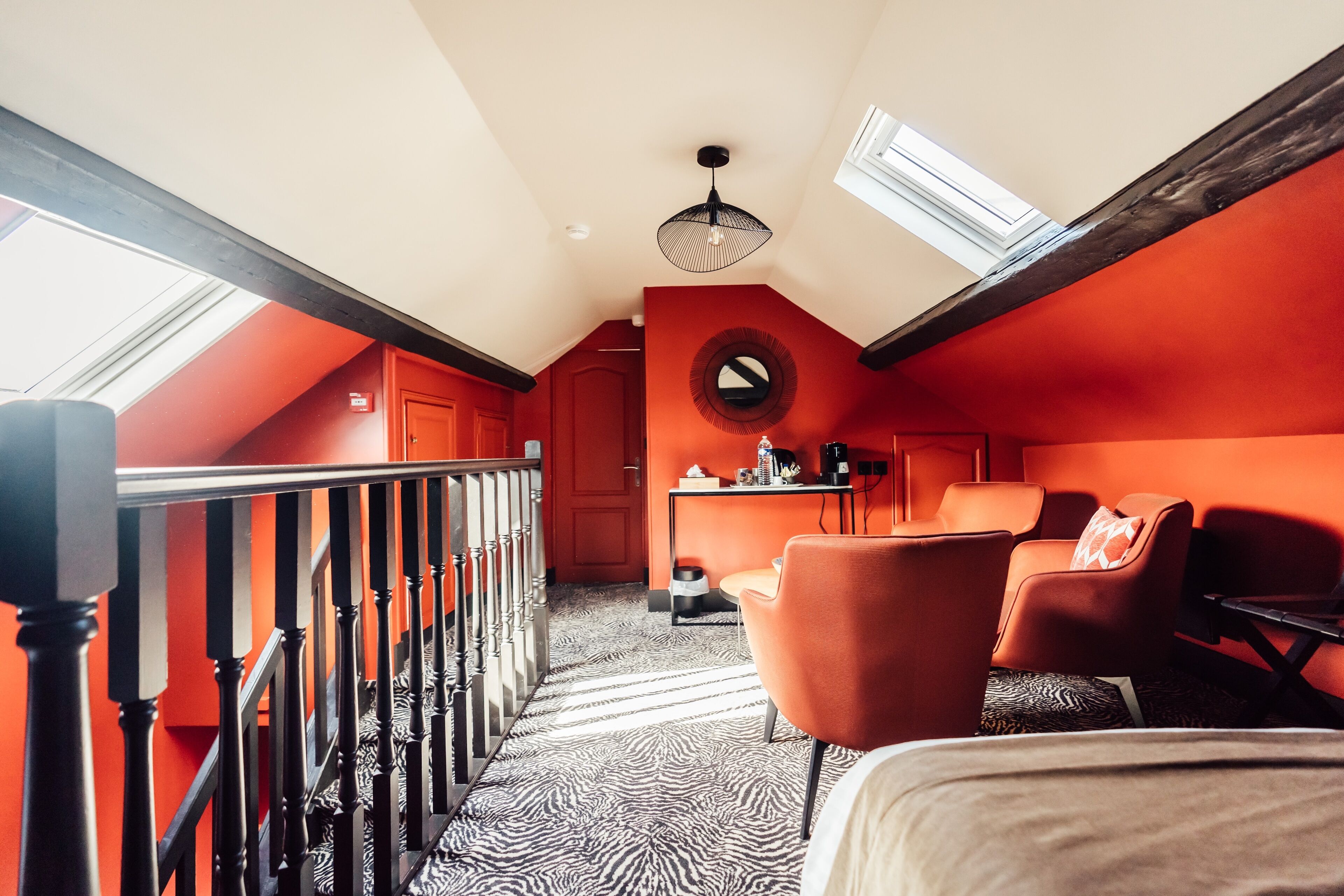 Una habitación con techo inclinado, una escalera, un espejo redondo y muebles color naranja.
