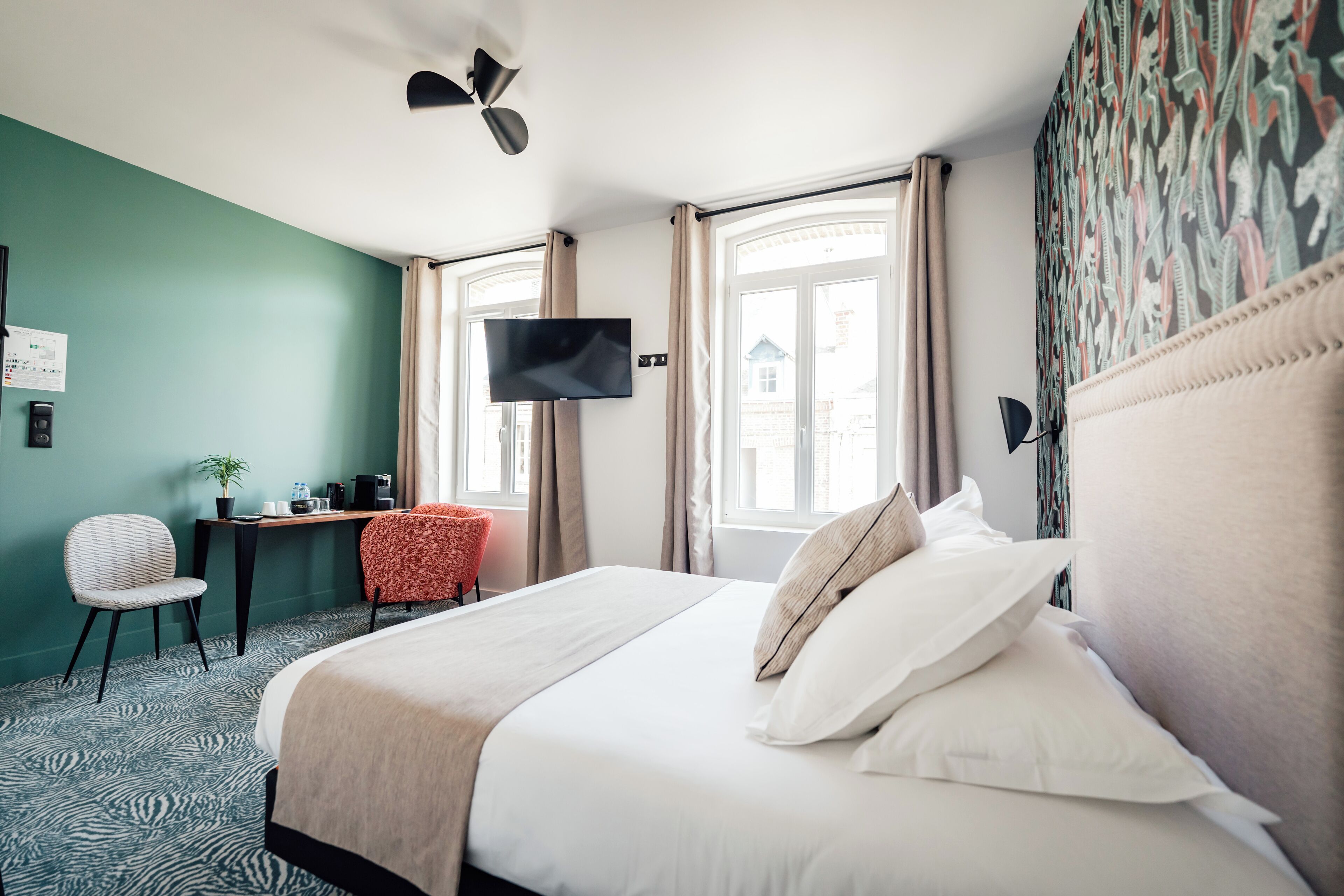 Habitación de hotel con cama, escritorio, silla, televisor y ventana con cortinas.