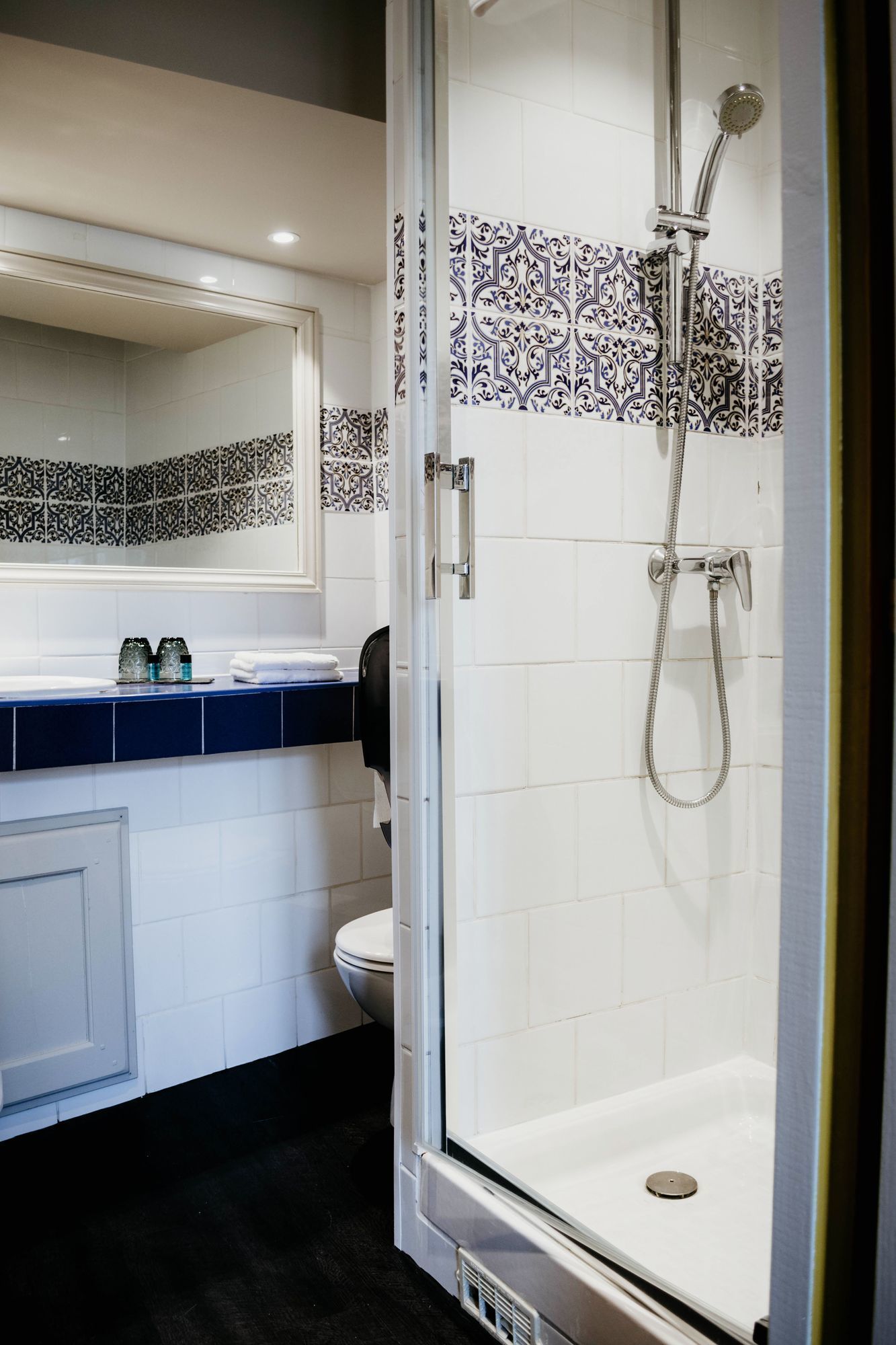 A modern bathroom with a glass-enclosed shower, a white toilet, and a blue-tiled vanity.
