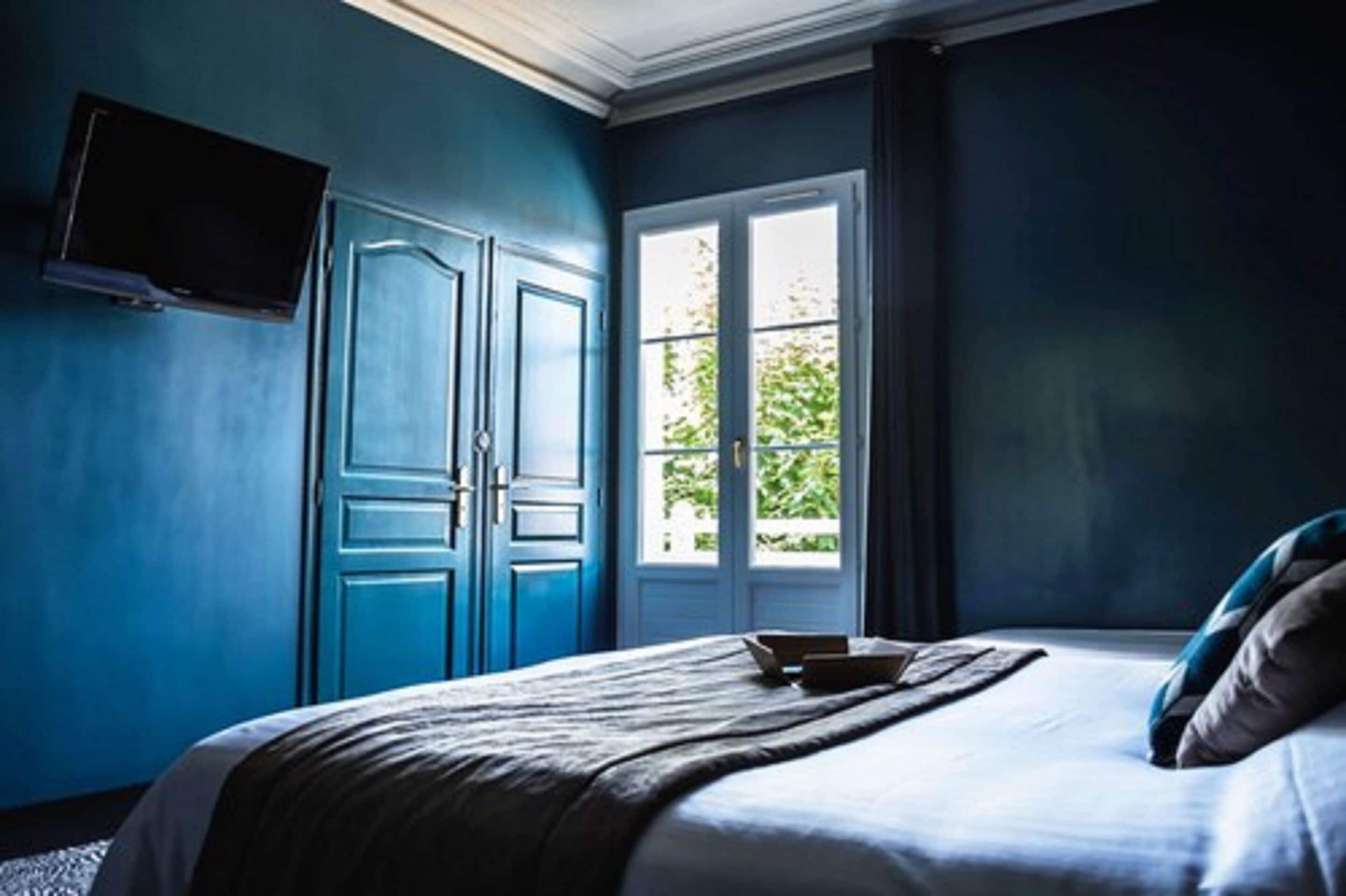 A bedroom with a bed, a television on the wall, and a window with a view of greenery.