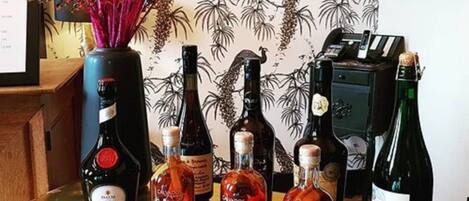 Una zona de bar con botellas de licores, un jarrón decorativo con flores rosadas y una pared con diseño de papel tapiz tropical.