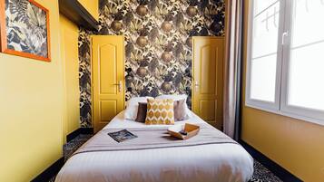A hotel room with a bed, yellow doors, a patterned wallpaper, and a window.