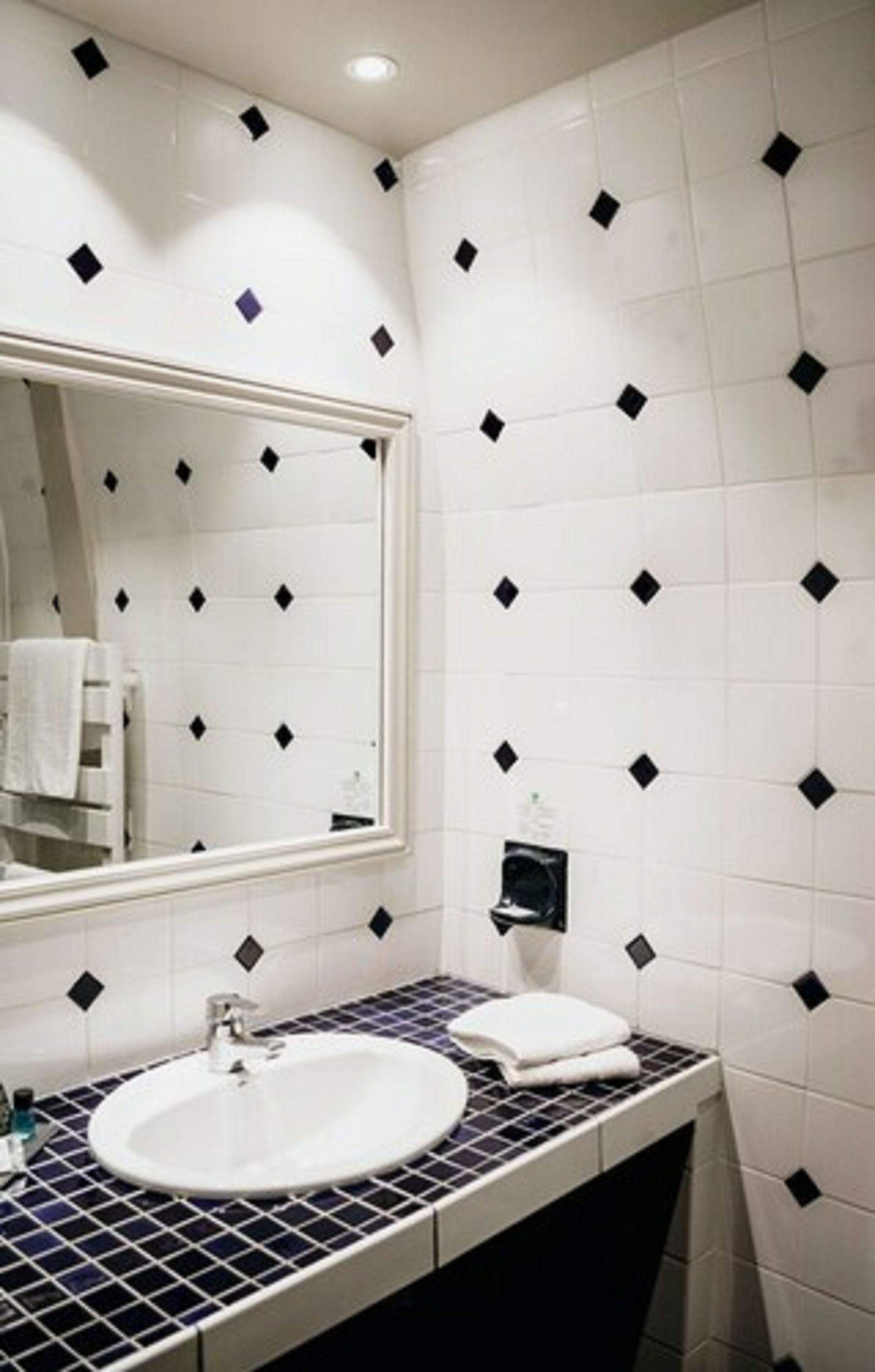 Un baño con un lavabo blanco, un espejo y una pared de azulejos con diseños de diamantes negros.