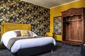 A bed with a headboard, a yellow armchair, a wooden wardrobe, and a patterned wall.