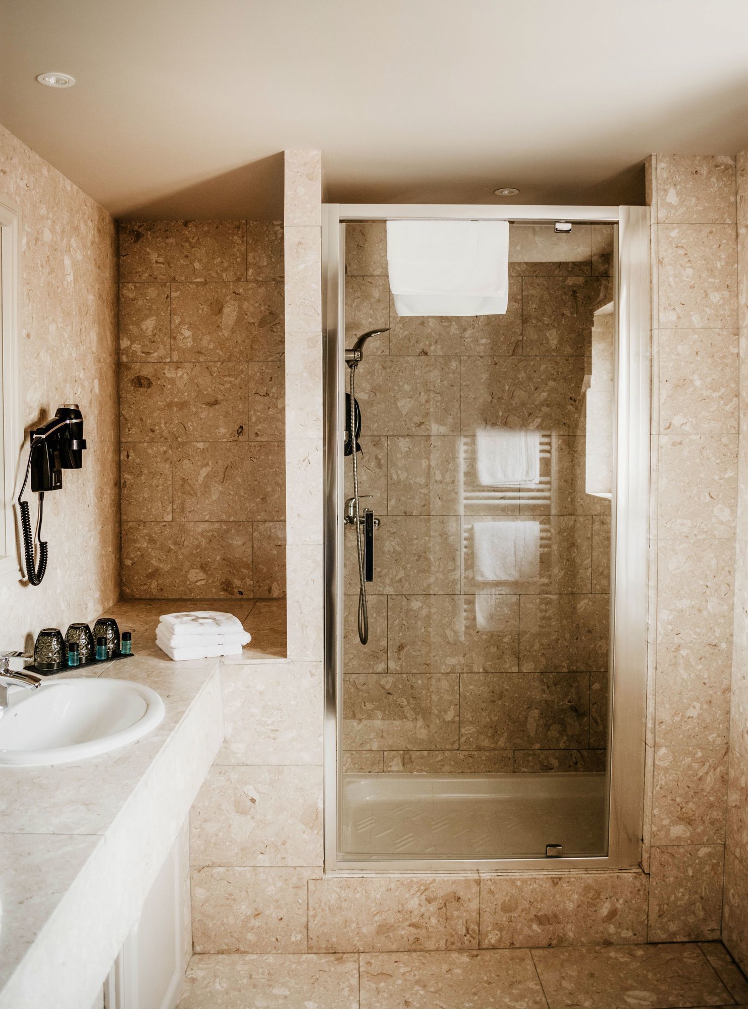 A modern bathroom with a glass-enclosed shower, a white sink, and a marble-tiled wall.