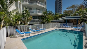 A swimming pool with blue lounge chairs, surrounded by a white fence and palm trees.