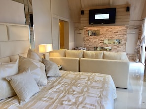 Ein modernes Hotelzimmer mit einem großen Bett, einer Couch, einem an der Wand montierten Fernseher und einer kleinen Küchenzeile mit Backstein-Spritzwand.