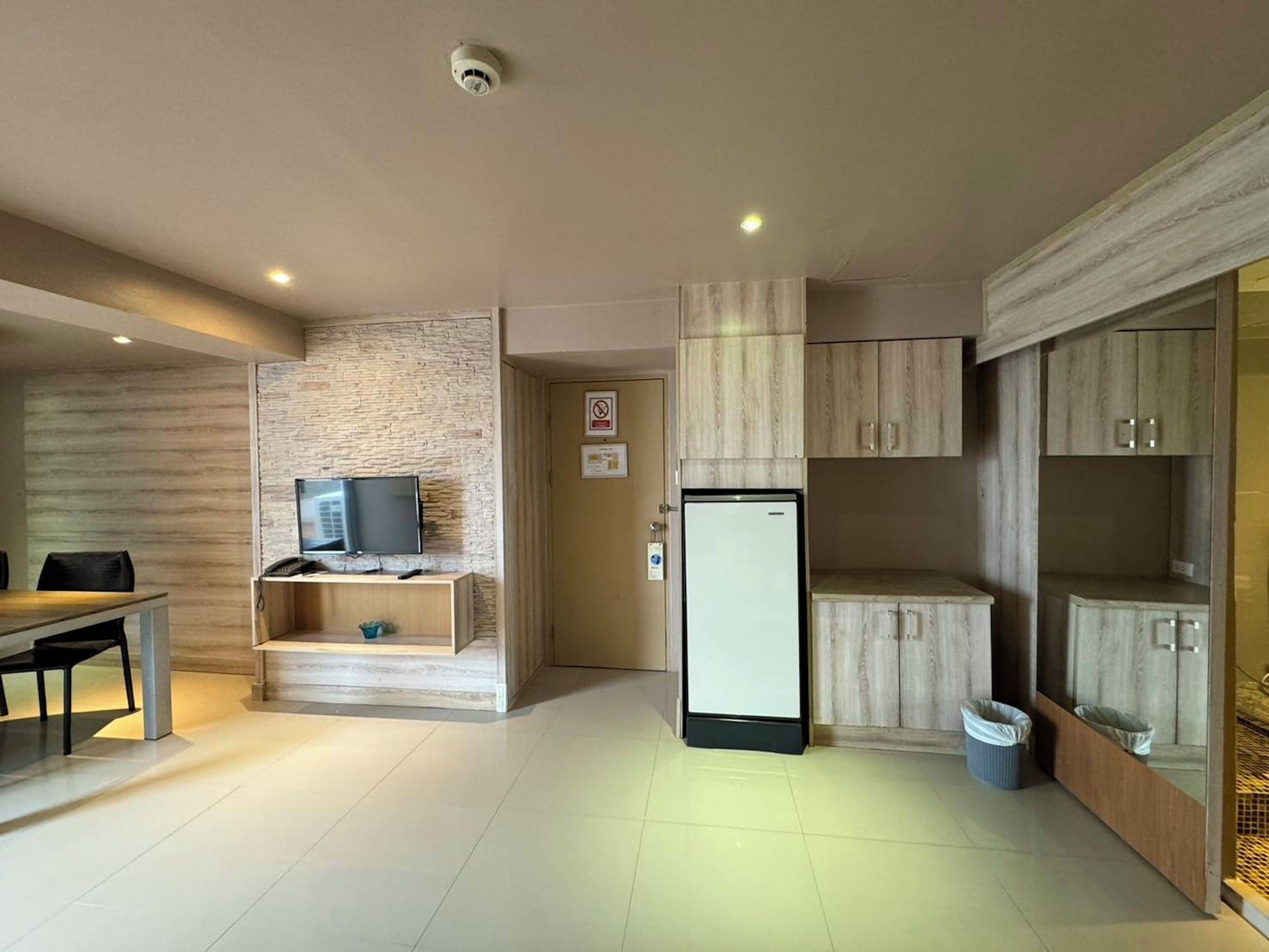 Una cocina moderna con un refrigerador empotrado, un pequeño rincón de descanso con una mesa y sillas, y un televisor sobre una estantería de madera.