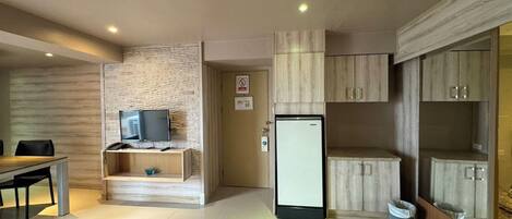 Una cocina moderna con un refrigerador empotrado, un pequeño rincón de descanso con una mesa y sillas, y un televisor sobre una estantería de madera.