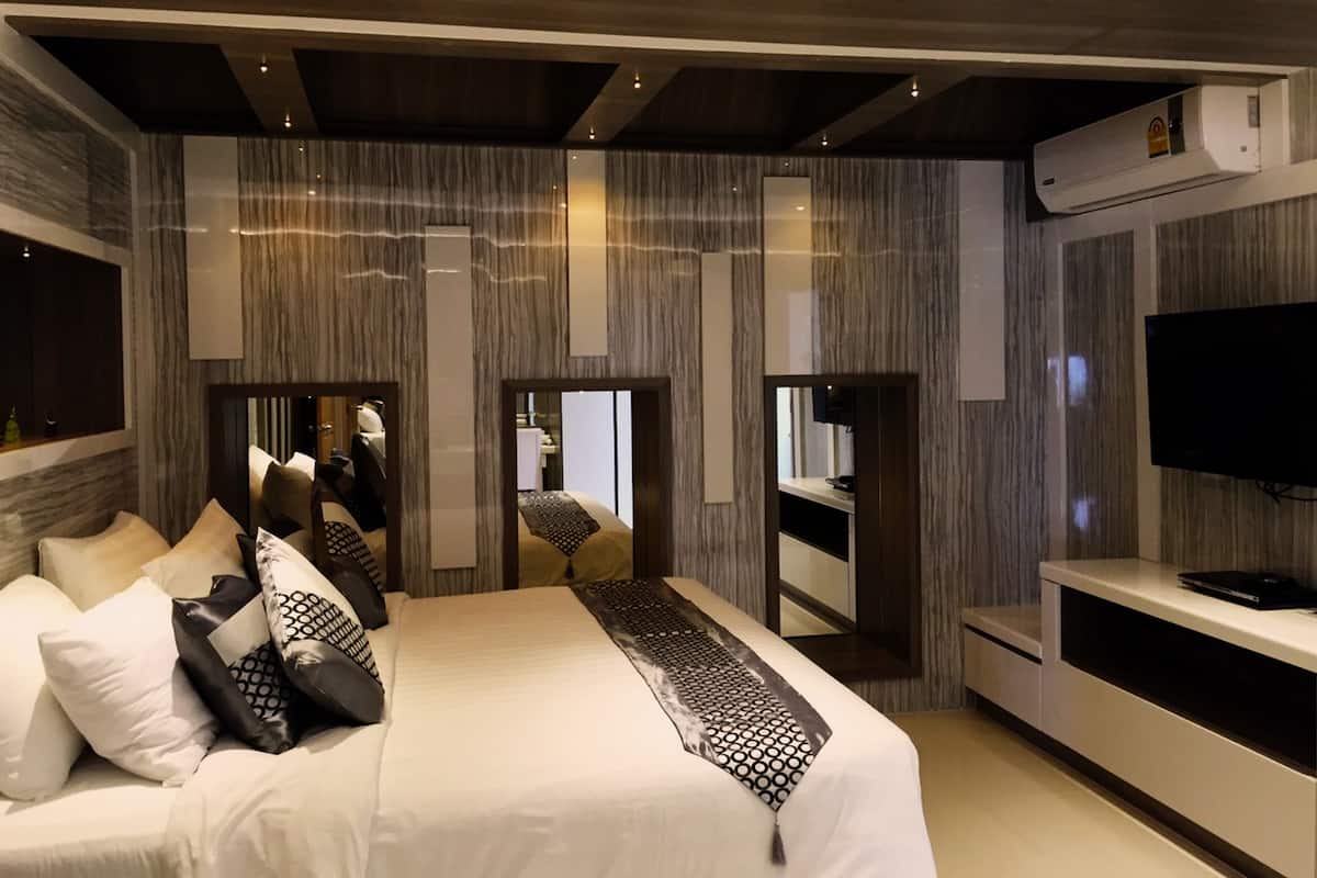 A modern hotel room with a large bed, a TV, and a mirror.