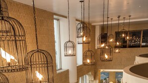 A spacious lounge area with wicker furniture, a large window offering a view of greenery, and hanging light fixtures.