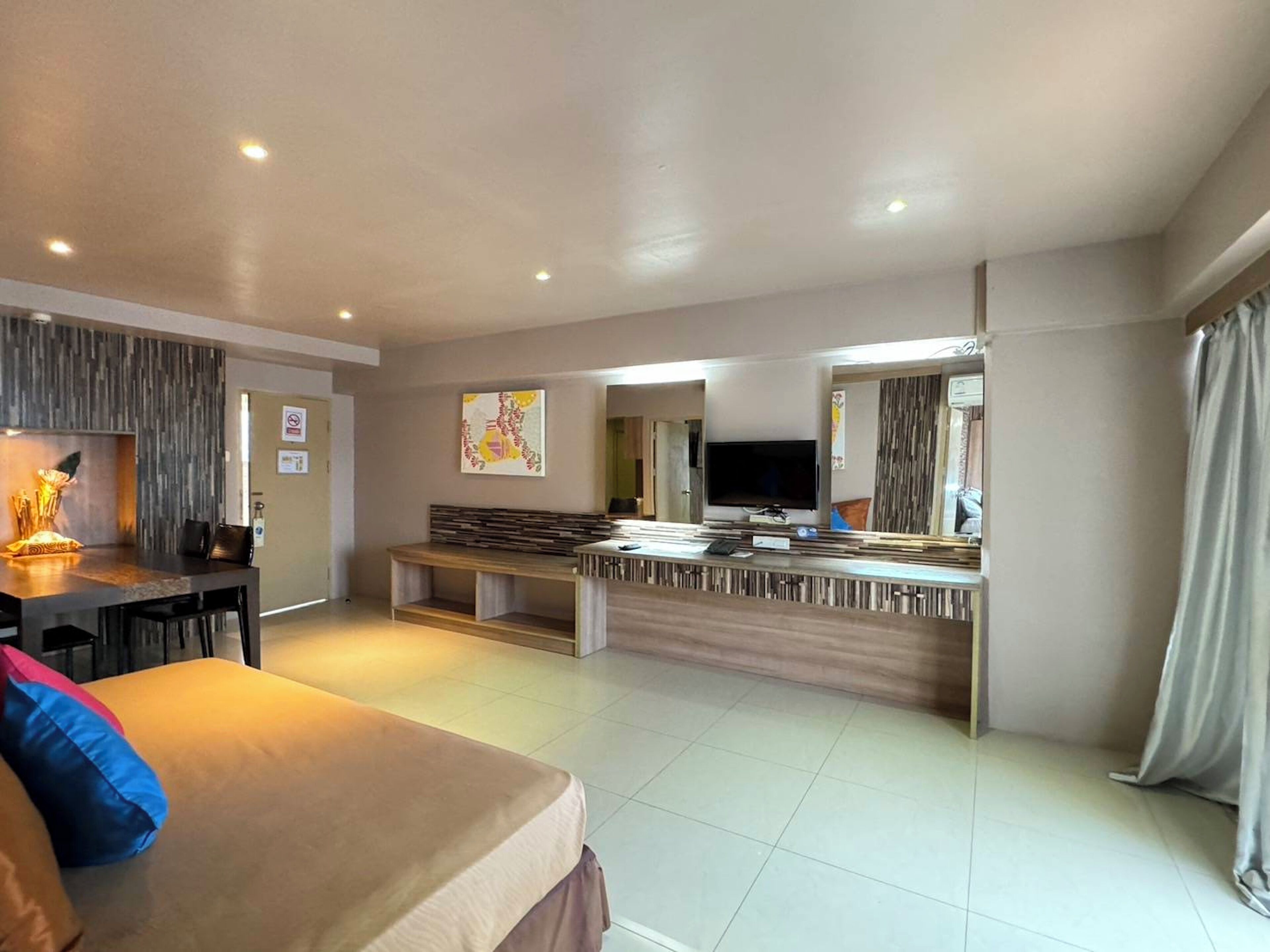 A modern hotel room with a large bed, a dining area with a TV, and a seating area with a view.