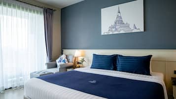 Une chambre d’hôtel avec un grand lit, une table de chevet, une lampe, une chaise et une fenêtre avec des rideaux.