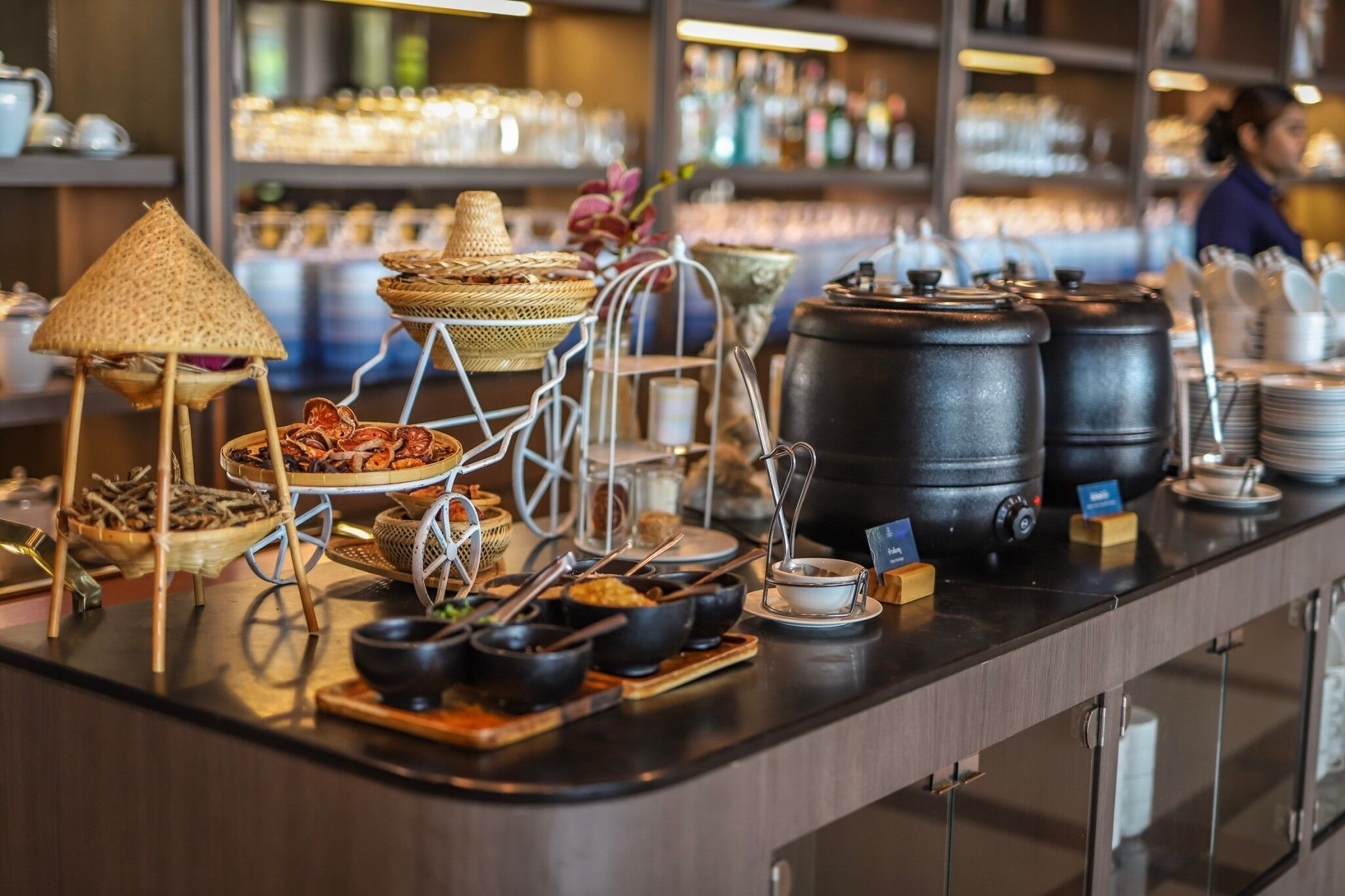 A buffet setup with various food items, a large black water dispenser, and a traditional straw hat.