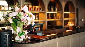 A reception desk with a floral arrangement, a cash register, and a shelf with bottles in the background. - The Cavalli Casa Resort (Ayutthaya)