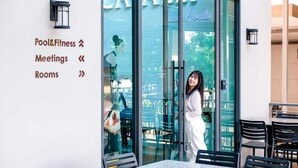 A hotel entrance with a glass door, a sign indicating amenities like Pool & Fitness, Meetings, and Rooms, and a person standing in front of the door. - The Cavalli Casa Resort (Ayutthaya)