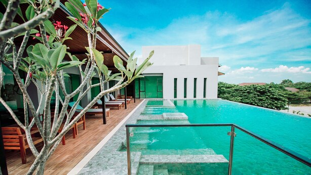 A pool area with clear water, steps leading into the pool, wooden deck, and a building with large windows. - The Cavalli Casa Resort (Ayutthaya)