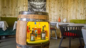 A wooden barrel with bottles of alcohol displayed inside, a green sofa, and a dining table with chairs in a rustic setting.