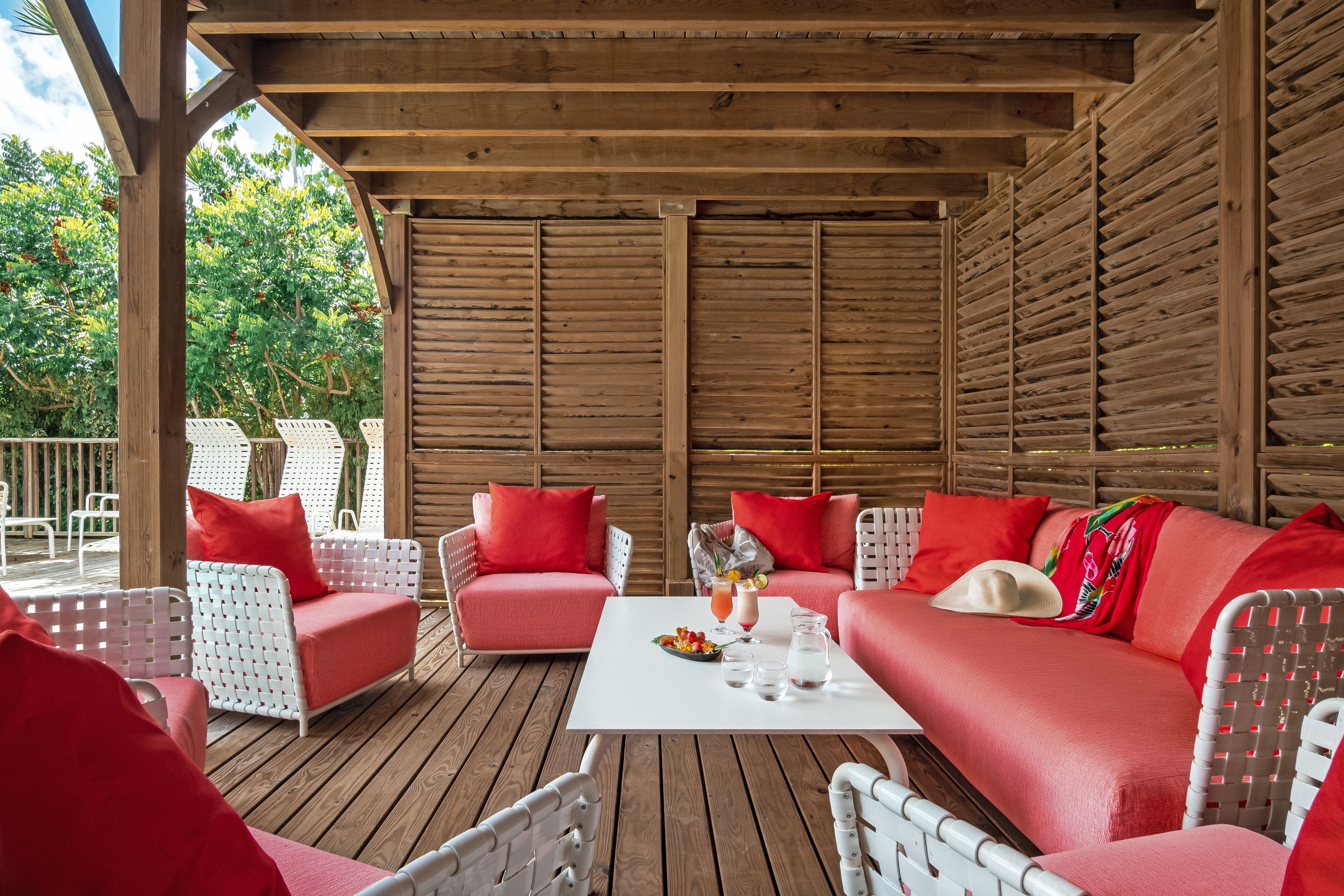 A covered outdoor seating area with wooden walls and white wicker furniture.