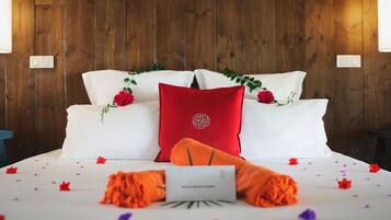 Een net opgemaakt bed met witte en rode kussens, een rood kussen met een bloemenprint, en oranje sierkussens.