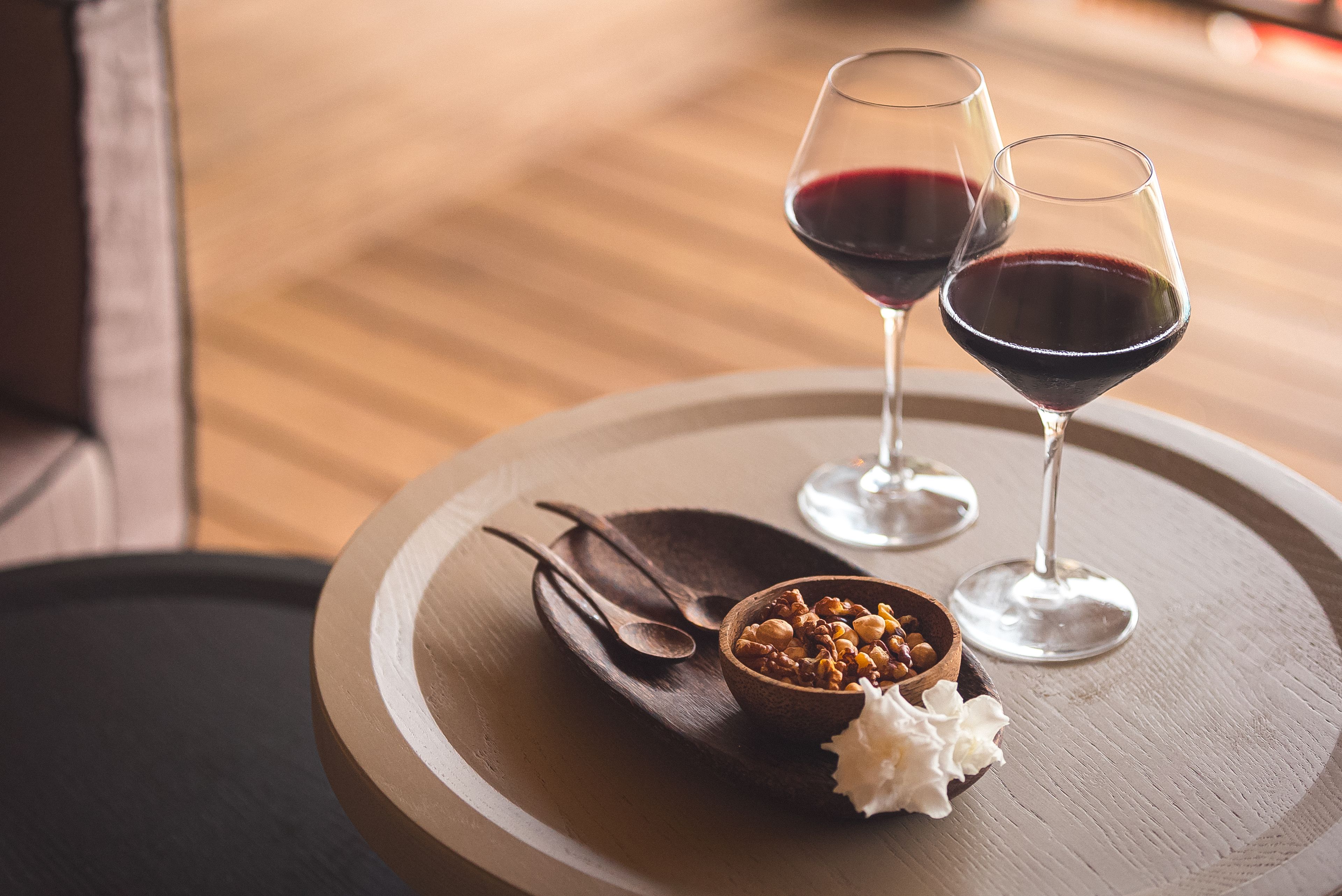 Two wine glasses on a wooden tray with a bowl of nuts and a dollop of cream.