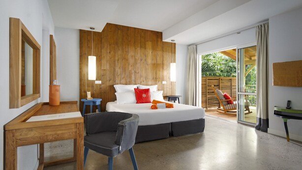 Une chambre moderne avec un grand lit, un mur revêtu de panneaux en bois et une porte-fenêtre coulissante donnant sur un balcon.