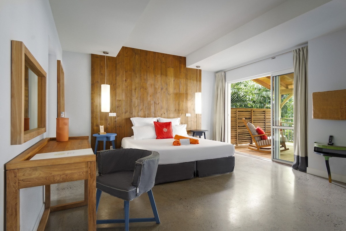 A modern bedroom with a large bed, wooden panel wall, and a sliding glass door leading to a balcony.