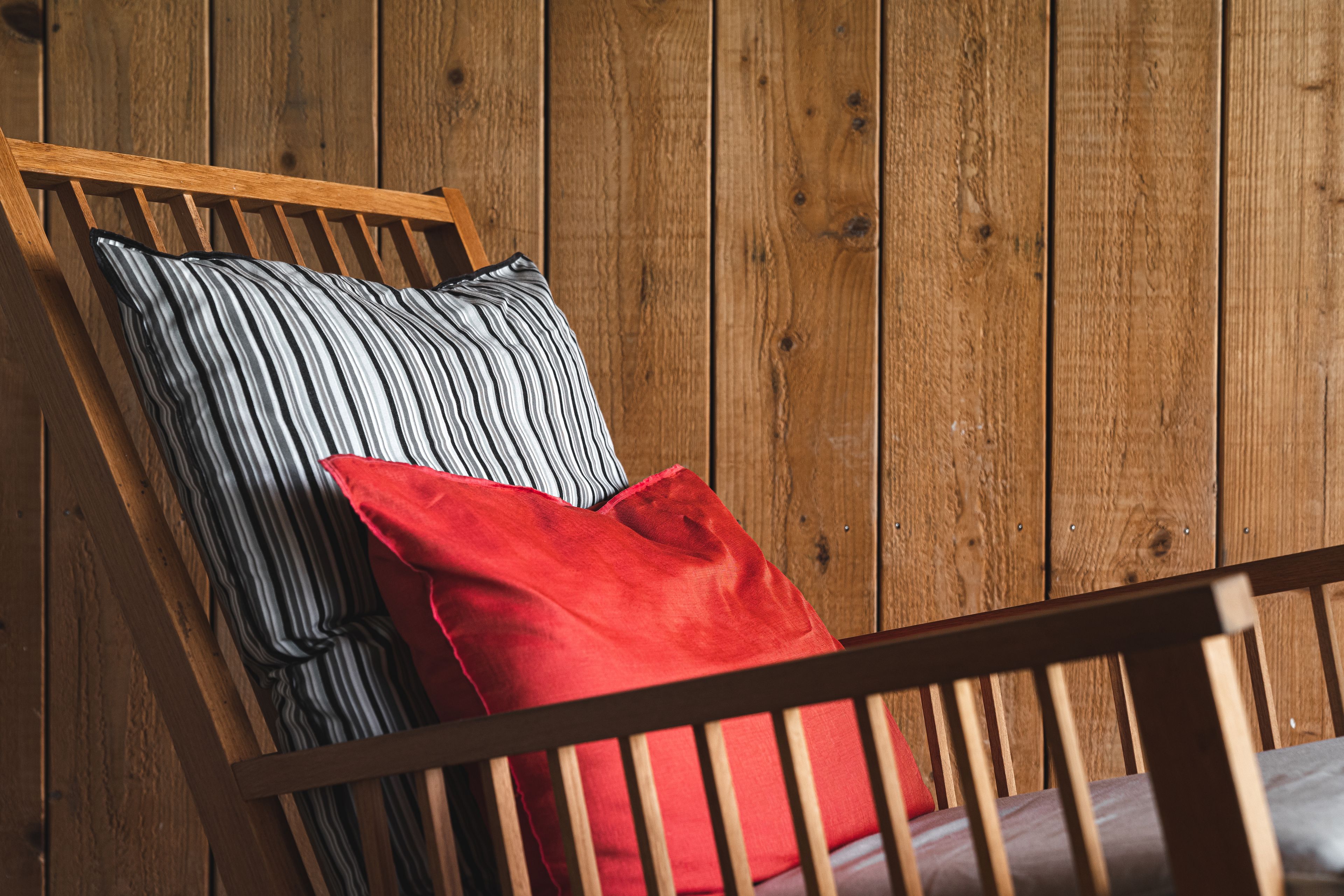 A wooden chair with a striped pillow and a red pillow against a wooden wall.