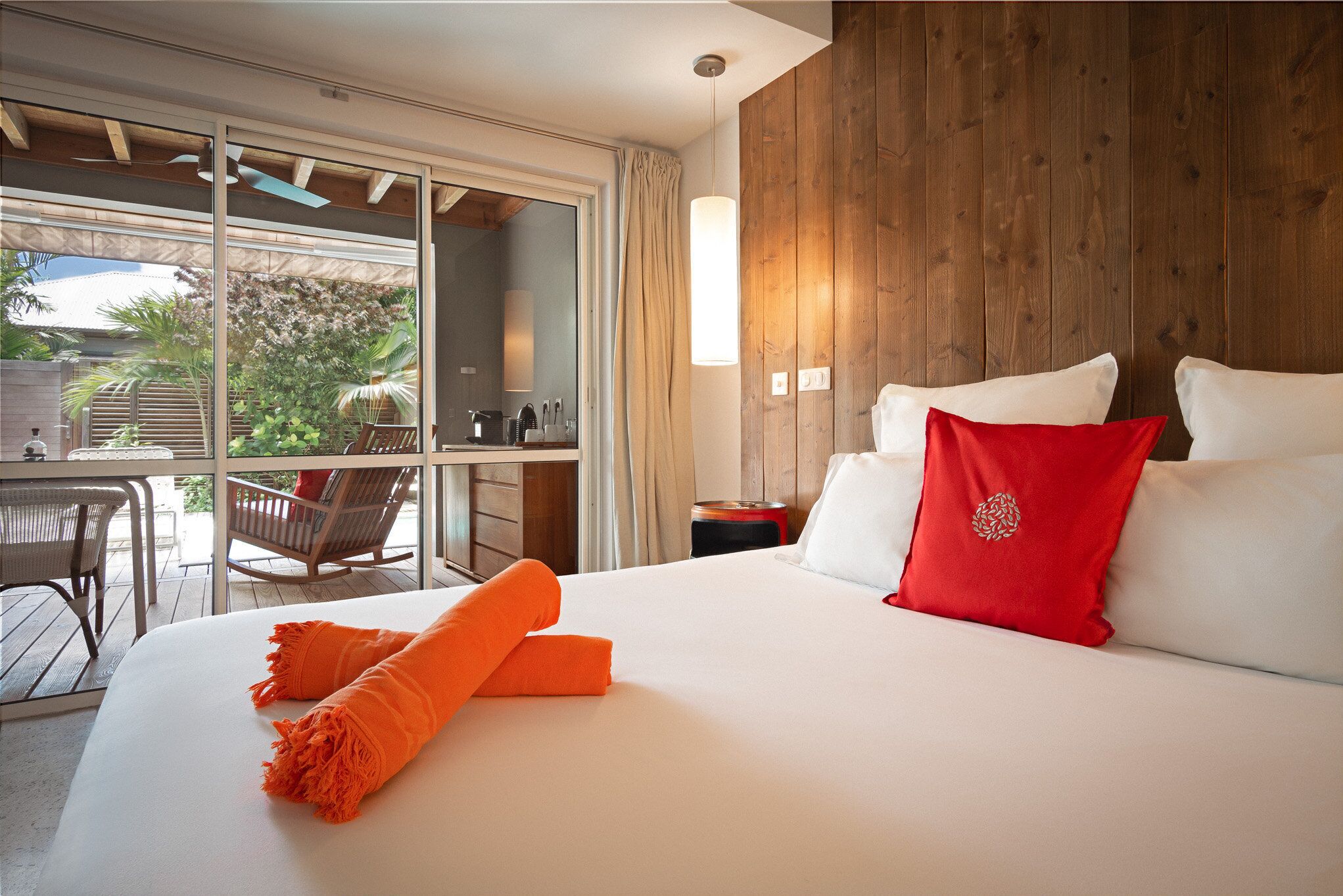 Een hotelkamer met een groot bed, een houten wand, een balkon met stoelen en uitzicht op groen.