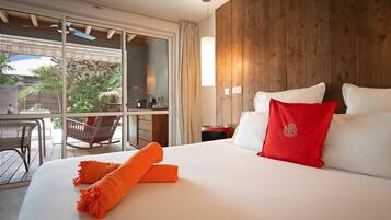 Een hotelkamer met een groot bed, een houten wand, een balkon met stoelen en uitzicht op groen.