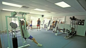 Ein Fitnessraum mit verschiedenen Trainingsgeräten, einem blauen Teppich und einer weißen Decke mit Leuchtstofflampen.