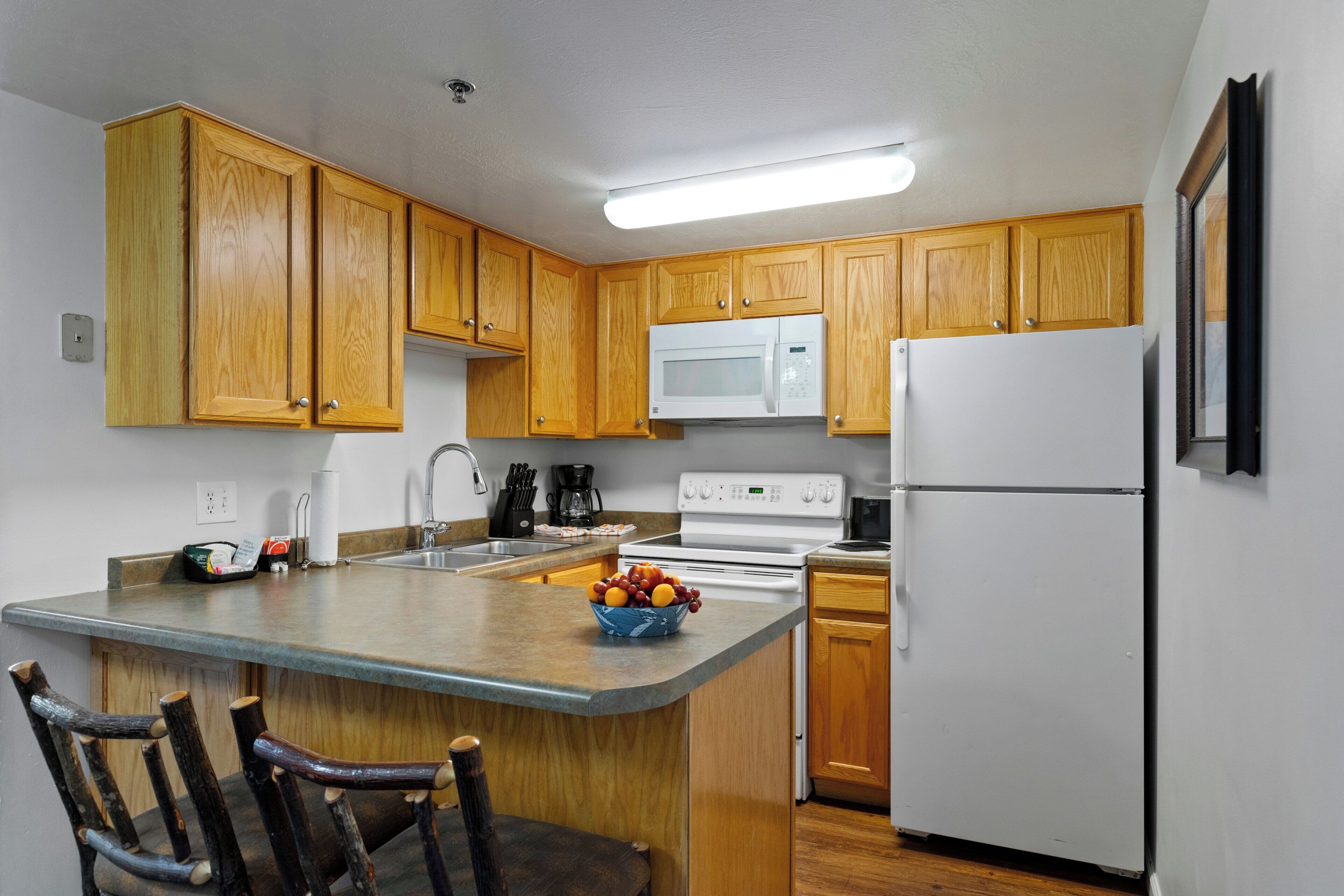 A kitchen with wooden cabinets, a white refrigerator, a microwave, a stove, and a sink.