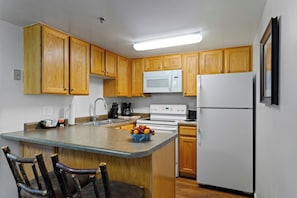 A kitchen with wooden cabinets, a white refrigerator, a microwave, a stove, and a sink. - WorldMark Wolf Creek (Eden)