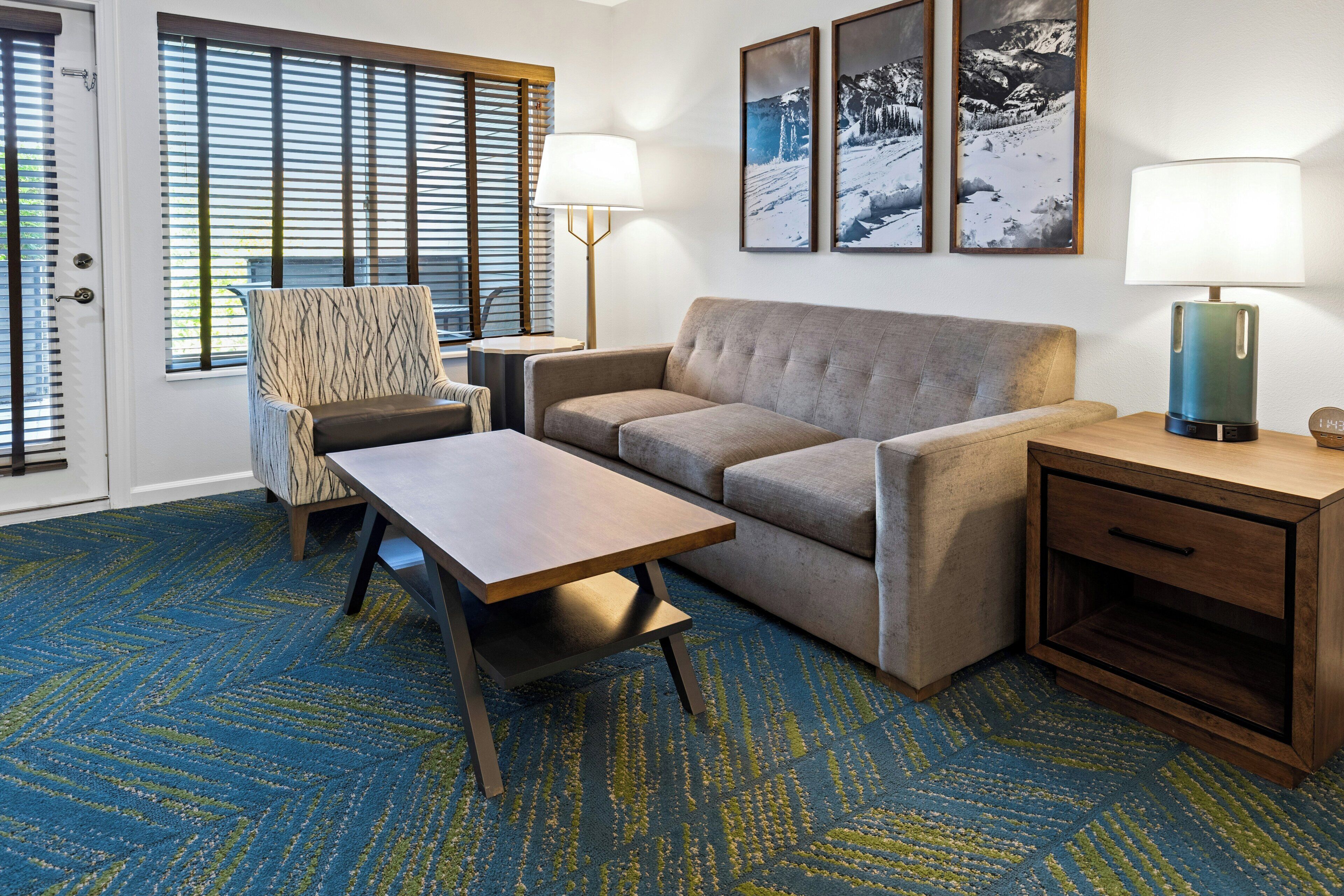 Ein Hotelzimmer mit Sofa, Sessel, Couchtisch und Schreibtisch mit Lampe.