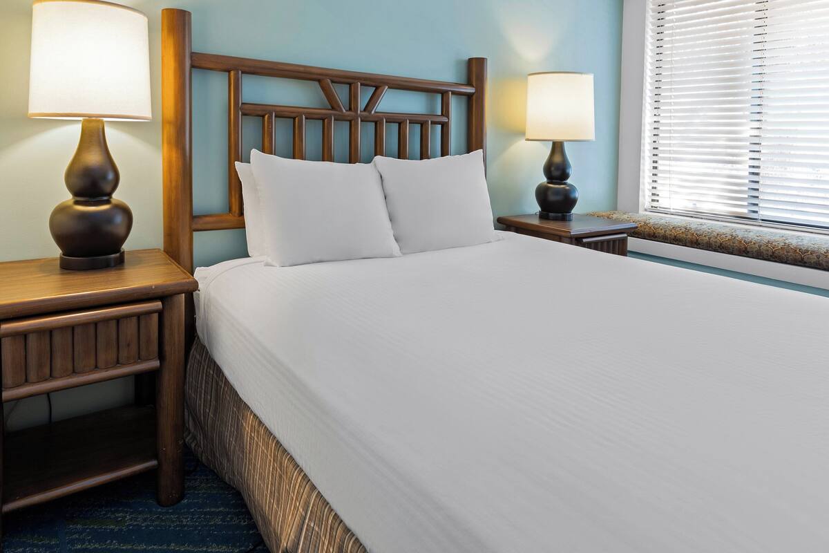 A neatly made bed with white linens, two bedside lamps, and a wooden headboard.