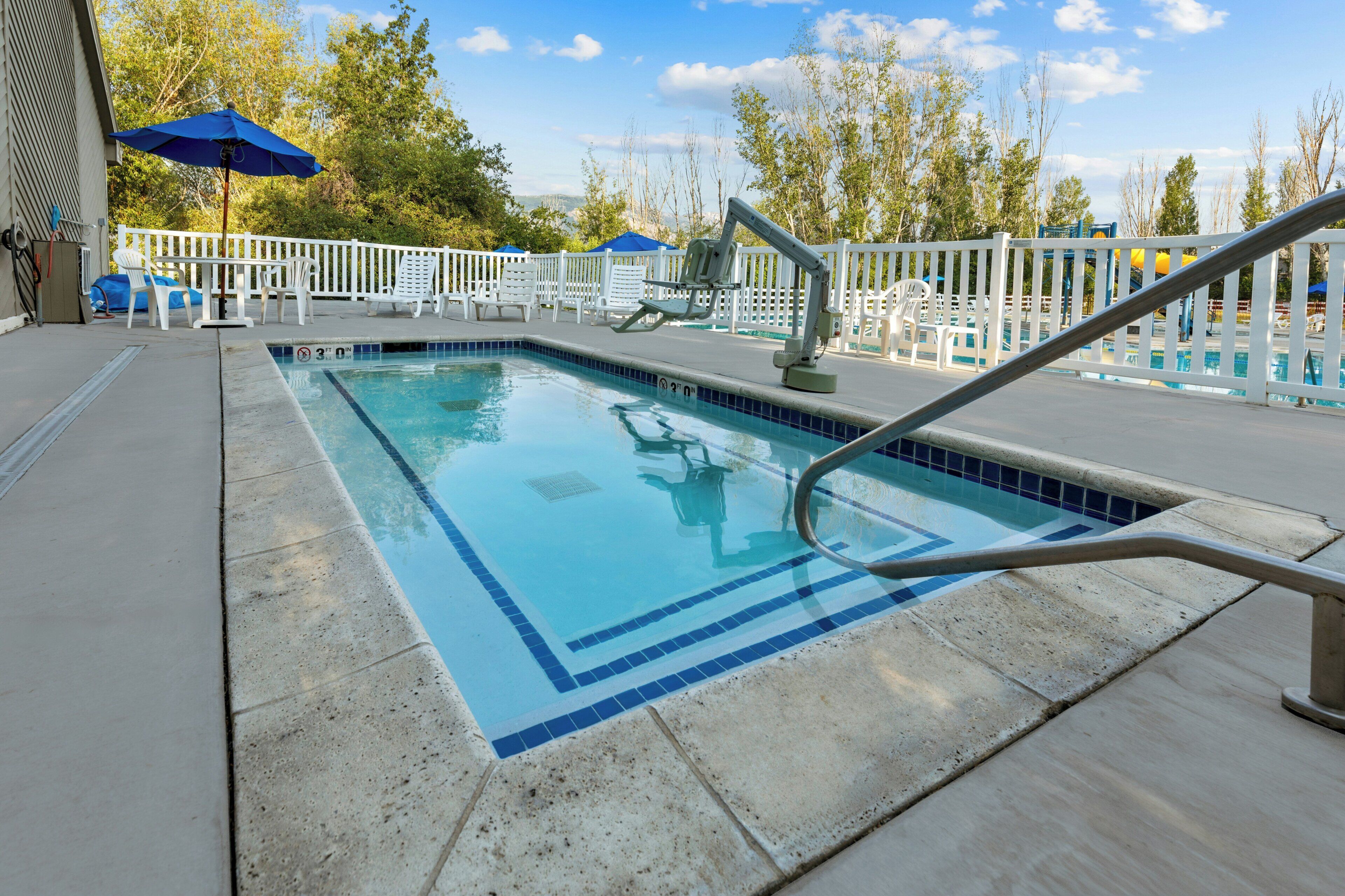 Ein Swimmingpool mit weißem Zaun, Liegestühlen und Sonnenschirmen.