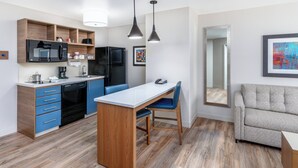Une cuisine moderne dotée d’appareils électroménagers intégrés, un coin repas avec un îlot central en bois et un canapé gris.