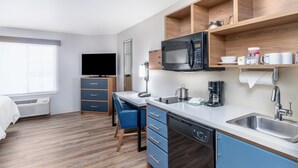 Une chambre d’hôtel compacte dotée d’une kitchenette, d’un téléviseur à écran plat, d’un bureau avec une chaise et d’une grande fenêtre.