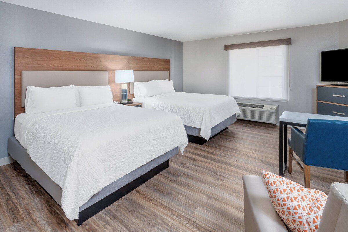 Een hotelkamer met twee bedden, een bureau met stoel, een televisie en een raam met jaloezieën.