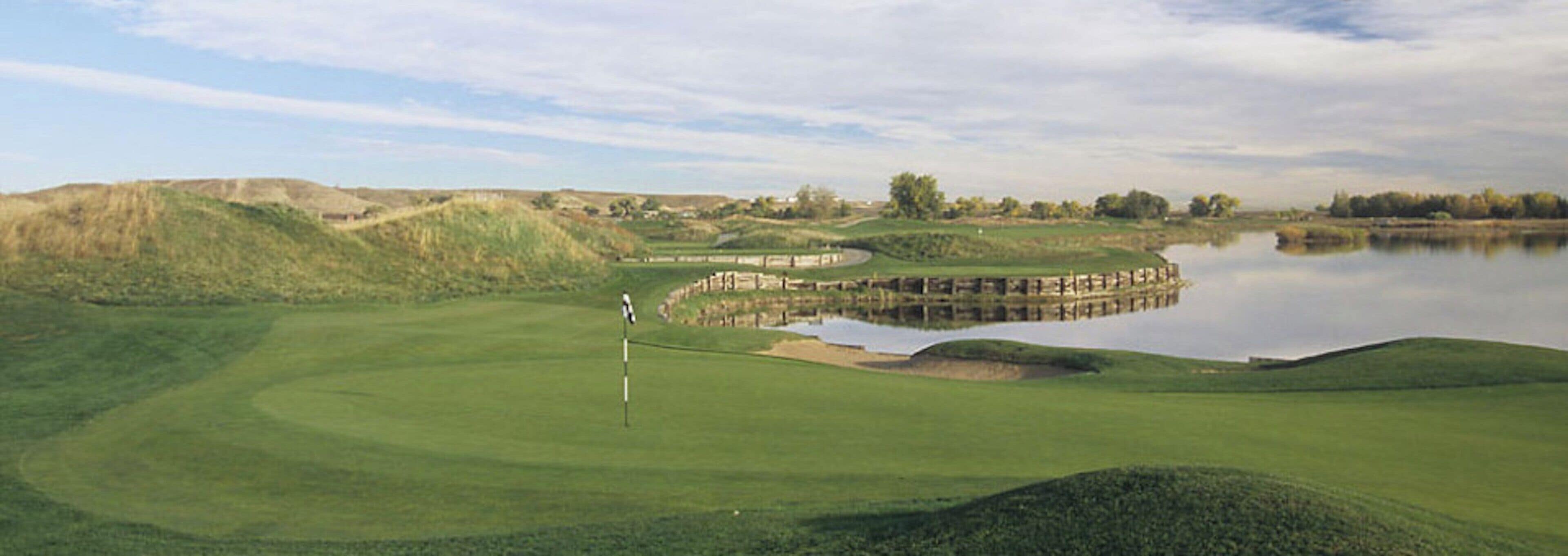 Campo de golfe com lago, bunkers de areia e haste de sinalização.