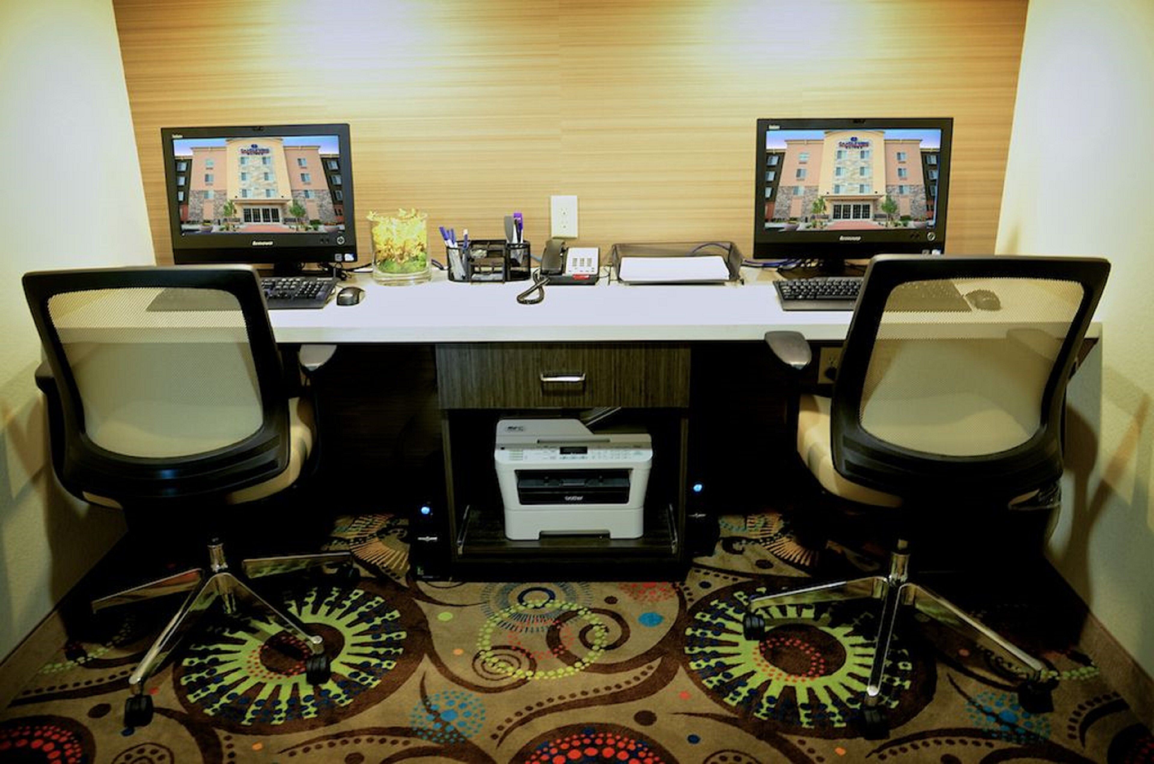 A hotel room with two desks, each with a computer and keyboard, a printer, and a small plant.