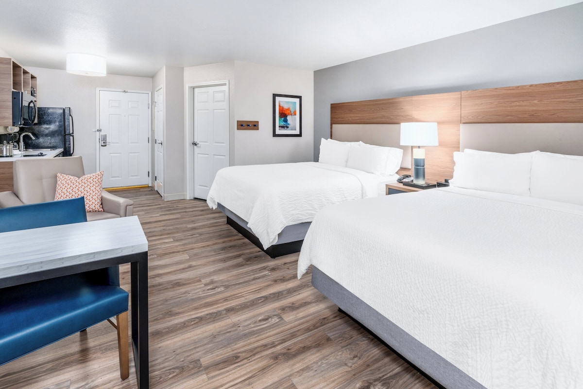 Een hotelkamer met twee bedden, een bureau, een stoel, een televisie en een deur naar de badkamer.