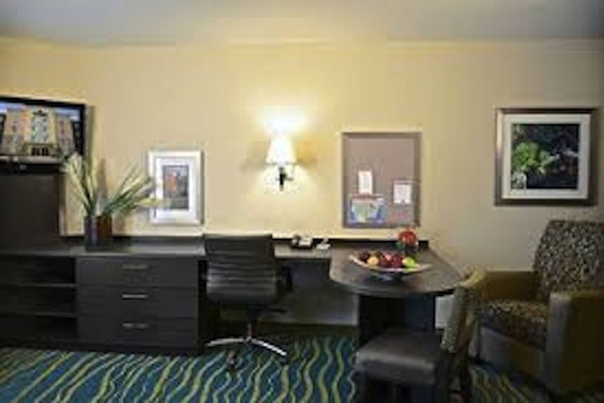 Hotelkamer met bureau, stoel en een klein tafeltje met fruit. Er hangt een lamp aan de muur en een ingelijst schilderij.