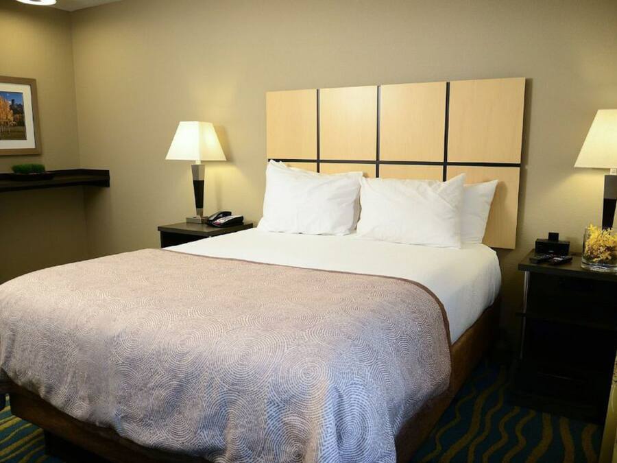 A hotel room with a large bed, two bedside tables with lamps, a nightstand with a phone, and a framed picture on the wall.