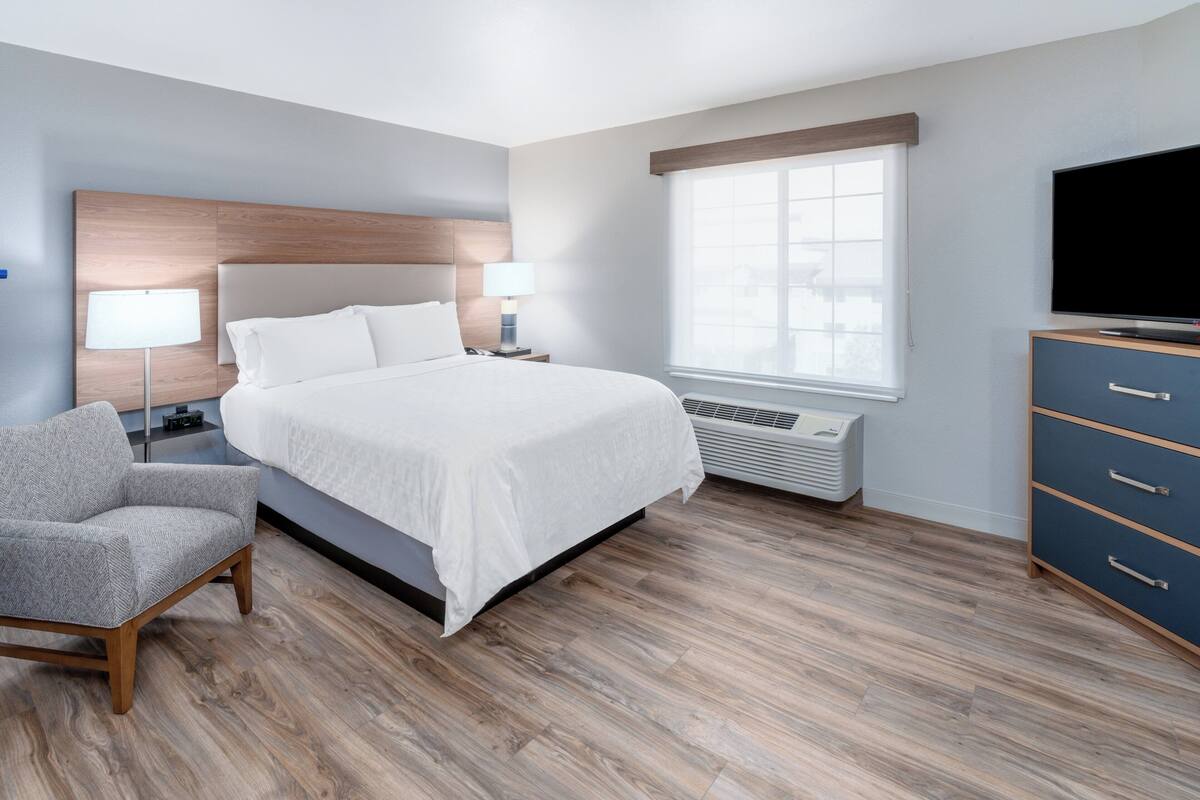 Een moderne hotelkamer met een groot bed, nachtlampjes, een flatscreen televisie, een dressoir en een raam met jaloezieën.